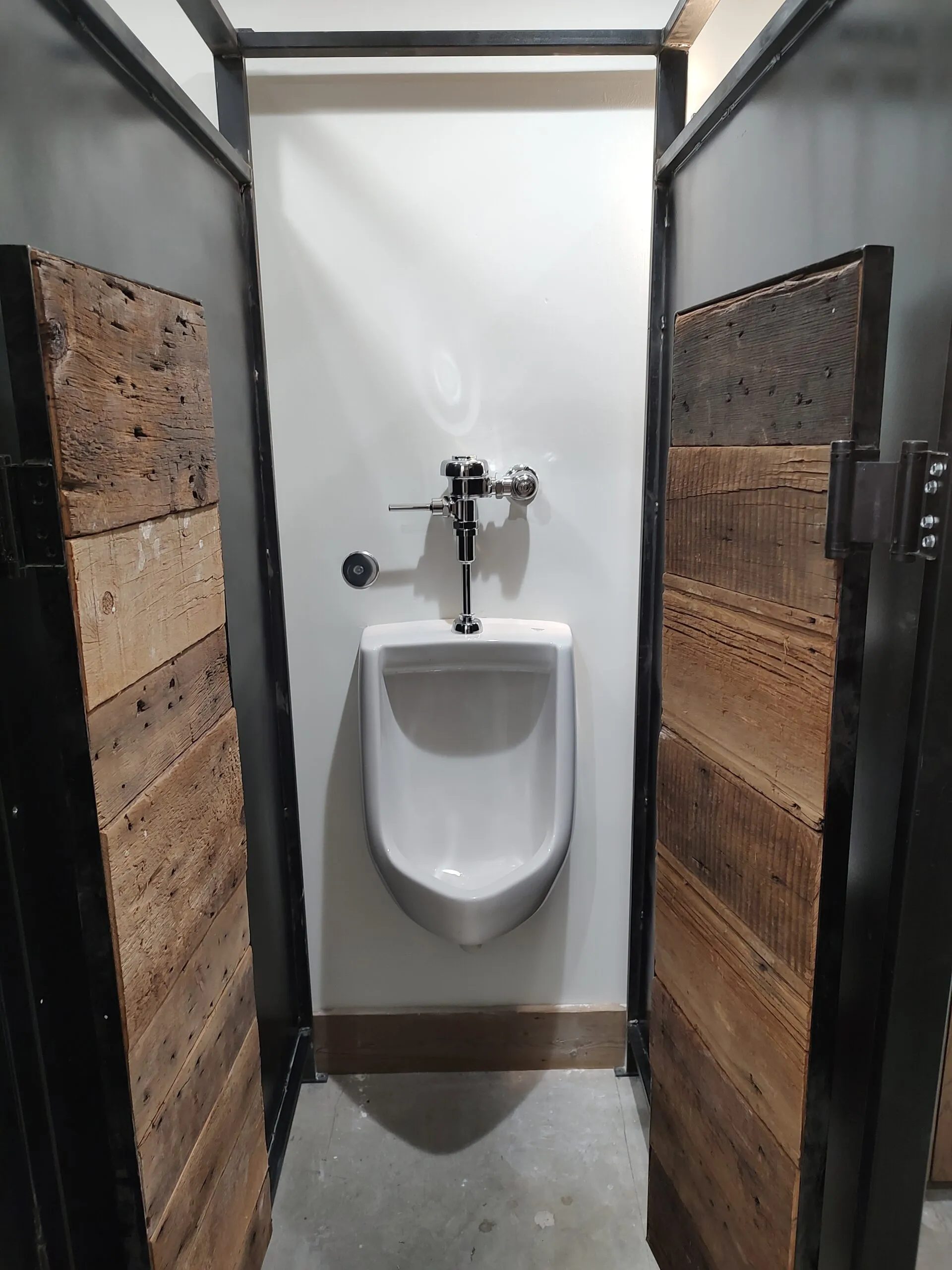 Commercial urinal between reclaimed barn wood partitions with black steel frames
